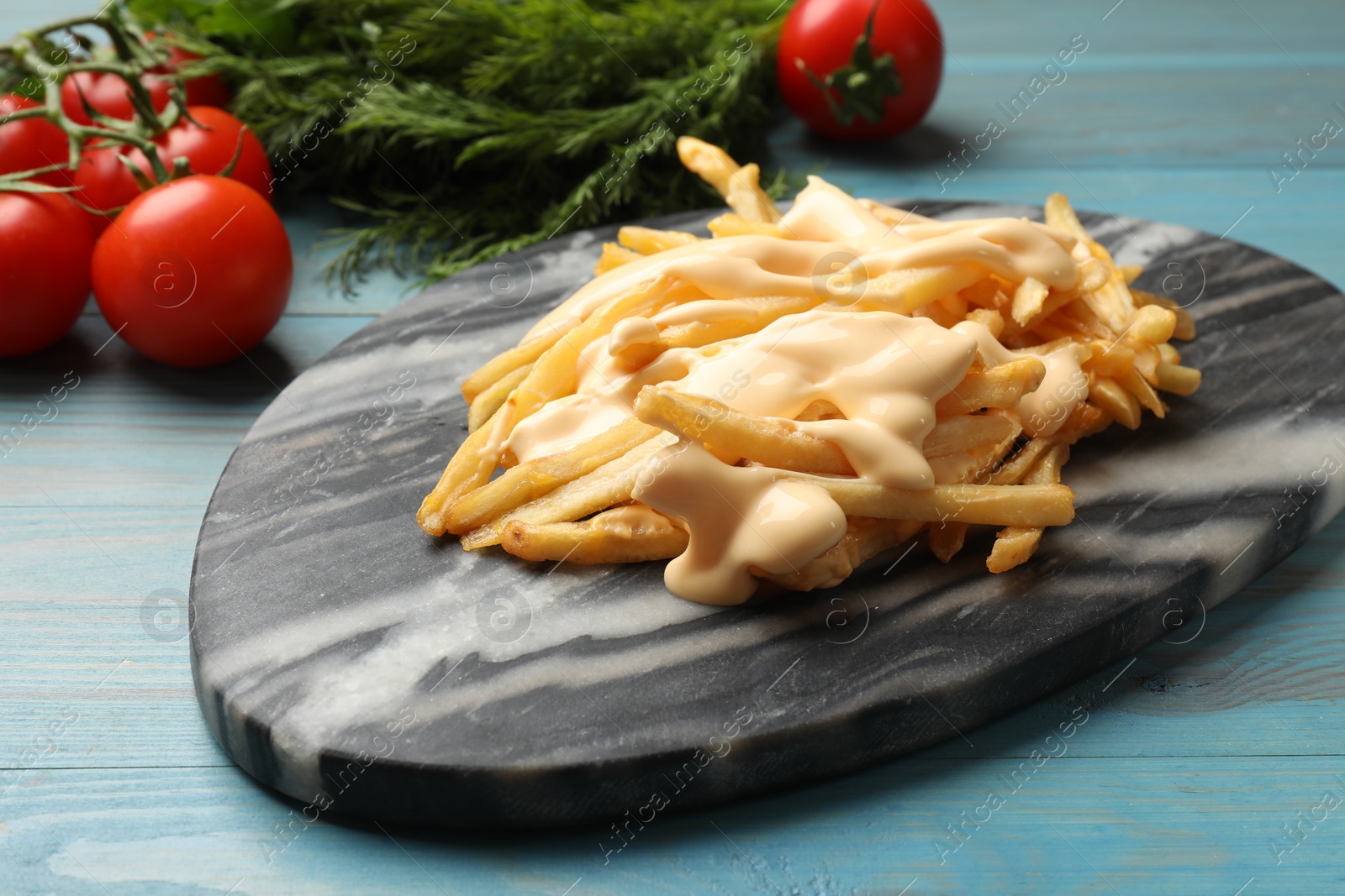 Photo of Delicious French fries with cheese sauce, tomatoes and dill on light blue wooden table, closeup