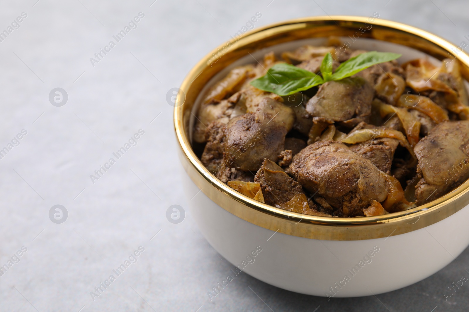 Photo of Delicious fried chicken liver with onion in bowl on light grey table, closeup. Space for text