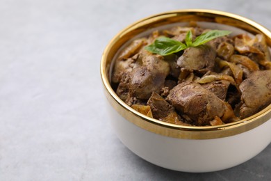 Delicious fried chicken liver with onion in bowl on light grey table, closeup. Space for text