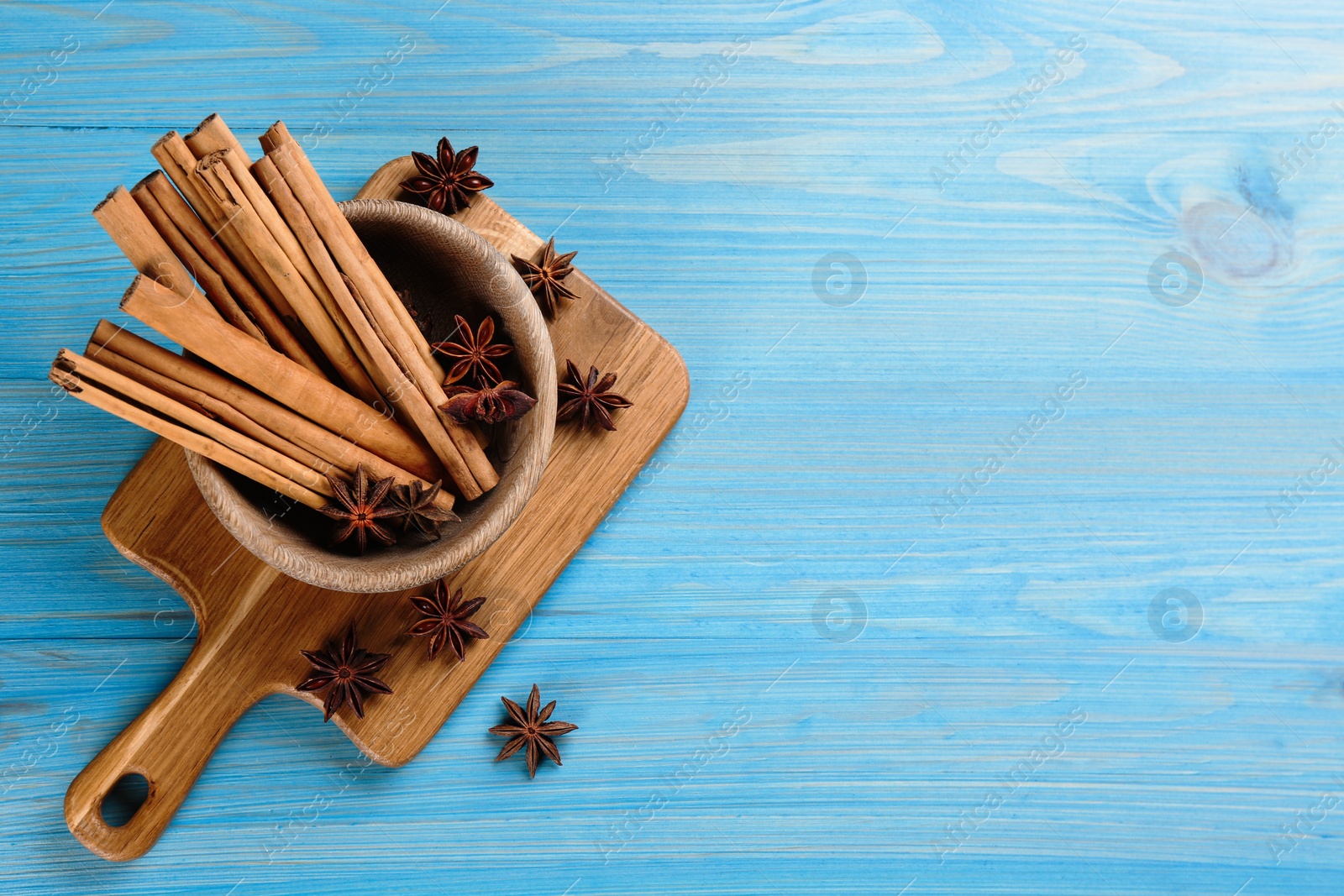 Photo of Aromatic cinnamon sticks and anise on light blue wooden table, flat lay. Space for text