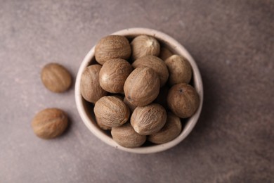 Photo of Whole nutmegs in bowl on brown table, top view