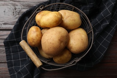 Raw fresh potatoes in metal basket on wooden table, top view