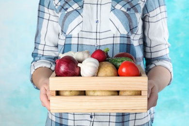Photo of Woman holding wooden crate with vegetables on color background, closeup