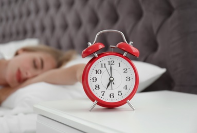 Analog alarm clock and blurred sleepy woman on background. Time of day