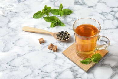Photo of Cup of hot aromatic mint tea and spoon with dry leaves on marble table