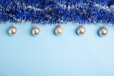 Photo of Bright tinsel and Christmas balls on light blue background, flat lay. Space for text