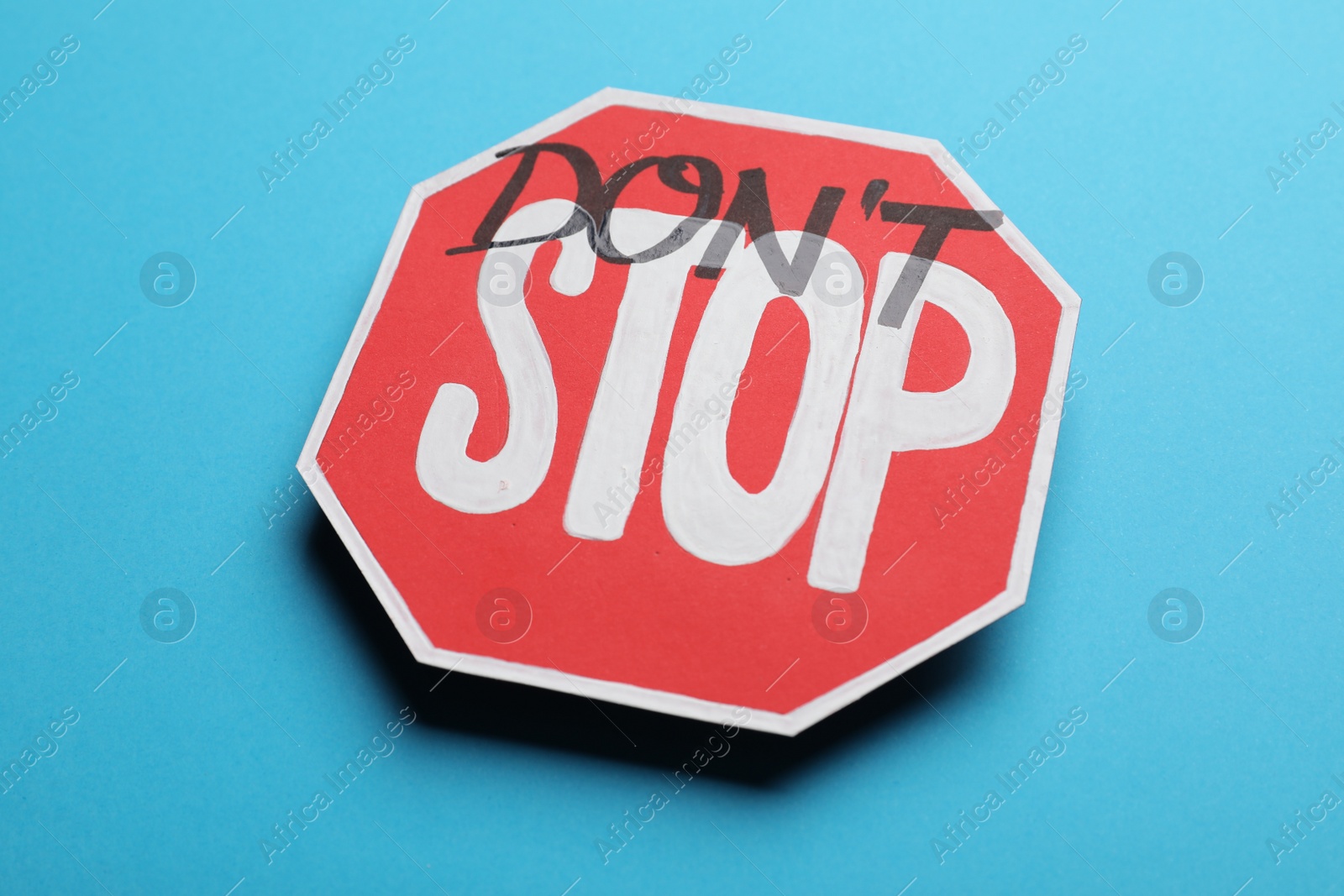 Photo of Don't stop - motivational phrase. Road sign sticker with added written text on light blue background