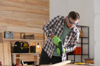 Photo of Carpenter working with electric drill at table indoors. Space for text
