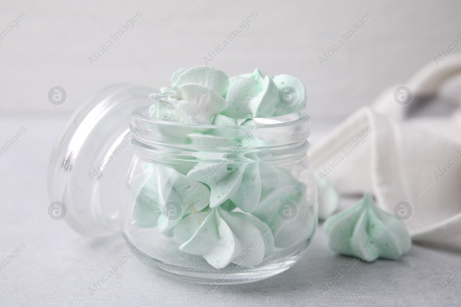 Photo of Tasty meringue cookies in glass jar on light grey table