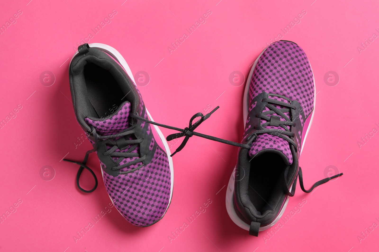 Photo of Stylish sneakers with black shoe laces on pink background, flat lay