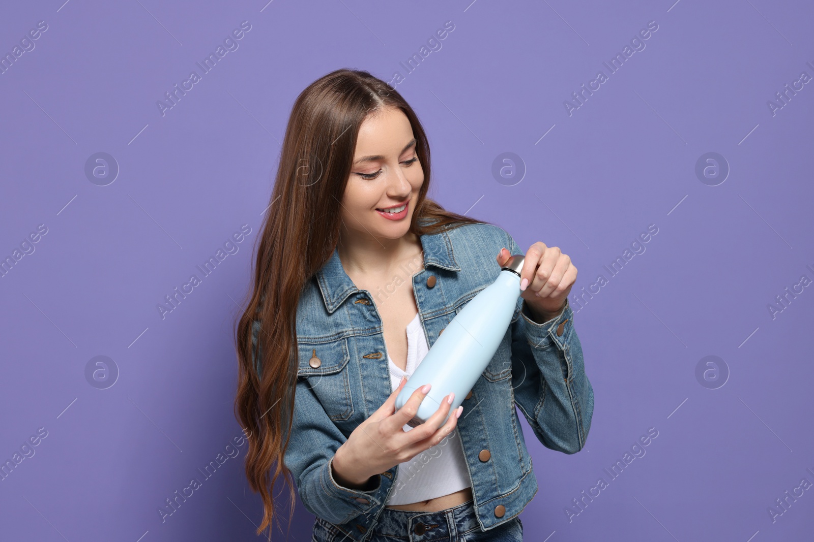 Photo of Beautiful young woman with thermos bottle on purple background