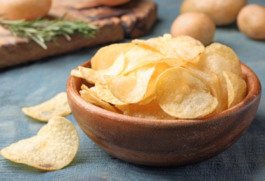Photo of Bowl of crispy potato chips on wooden table