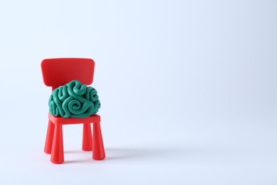 Photo of Brain made of plasticine on mini chair against white background. Space for text