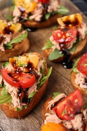 Photo of Delicious bruschettas with balsamic vinegar, tomatoes, arugula and tuna on wooden table, closeup
