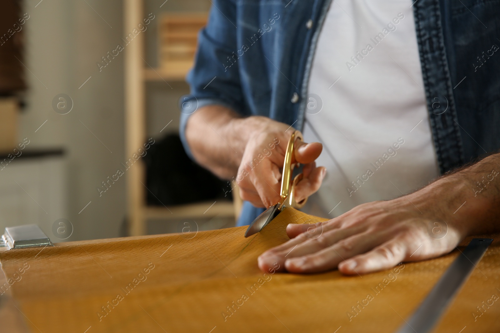 Photo of Man cutting leather with scissors in workshop, closeup