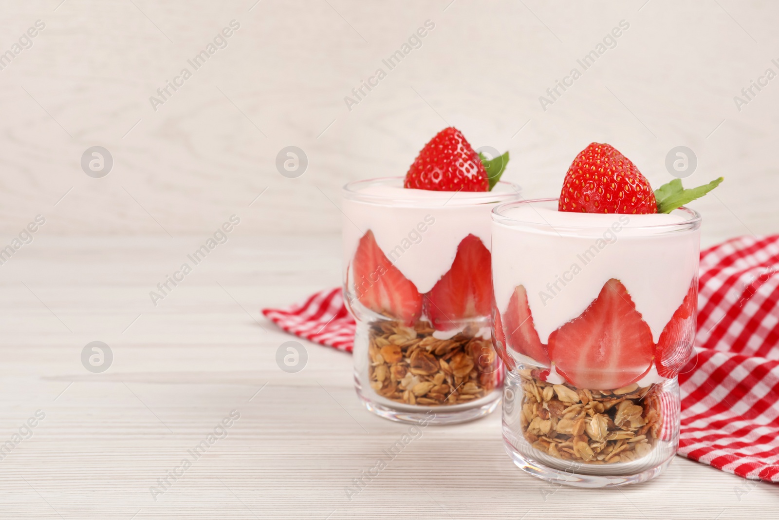 Photo of Glasses of tasty yogurt with muesli and strawberries served on white wooden table, space for text