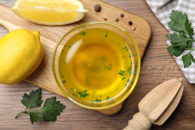 Photo of Bowl with lemon sauce and ingredients on wooden table, flat lay. Delicious salad dressing