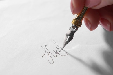 Photo of Woman signing on sheet of paper with fountain pen, closeup