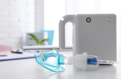 Photo of Modern nebulizer with child mask on white table indoors. Equipment for inhalation