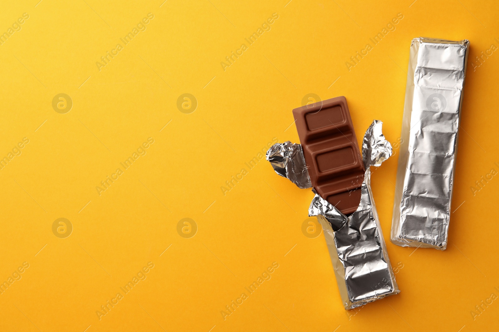 Photo of Tasty chocolate bars wrapped in foil on yellow background, flat lay. Space for text