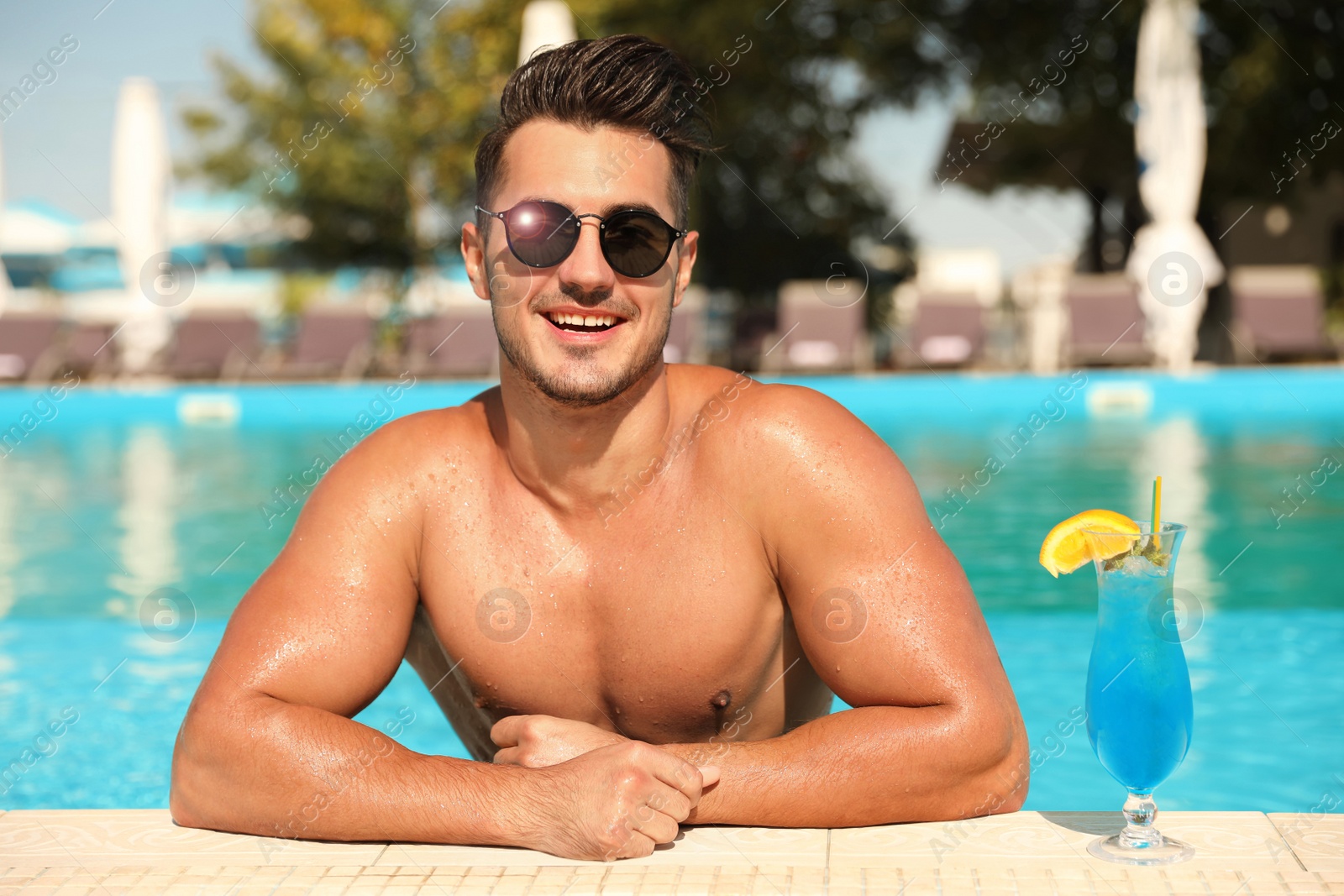 Image of Young man with cocktail in pool on sunny day