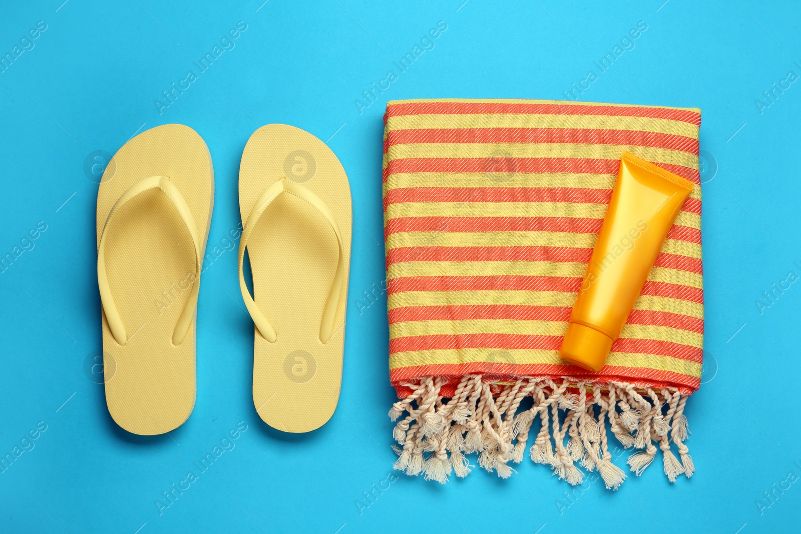 Photo of Beach towel, flip flops and sun protection product on light blue background, flat lay