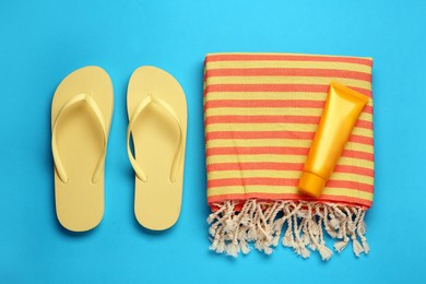 Beach towel, flip flops and sun protection product on light blue background, flat lay