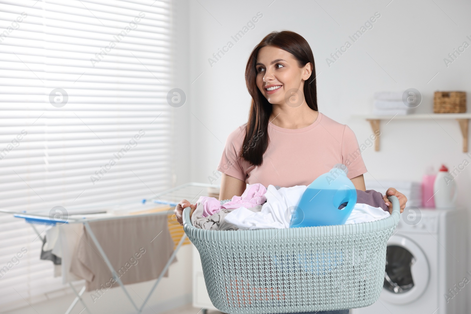 Photo of Woman holding basket with dirty clothes and fabric softener in bathroom, space for text