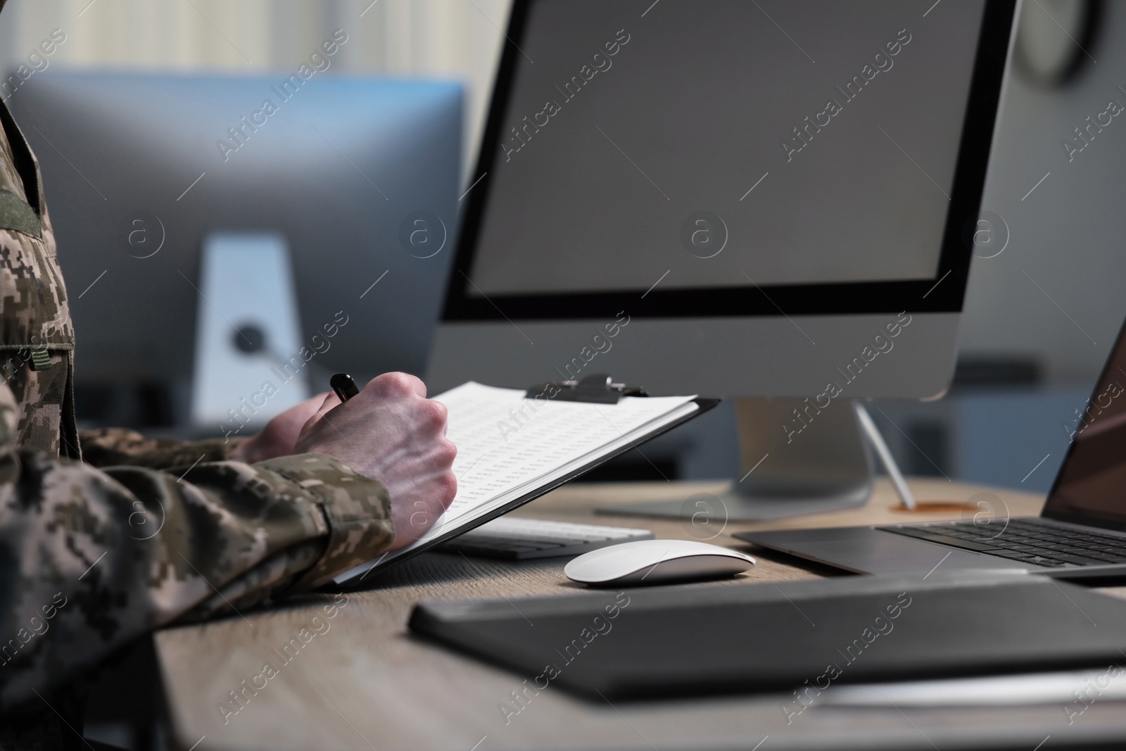 Photo of Military service. Soldier with clipboard working at wooden table in office, closeup