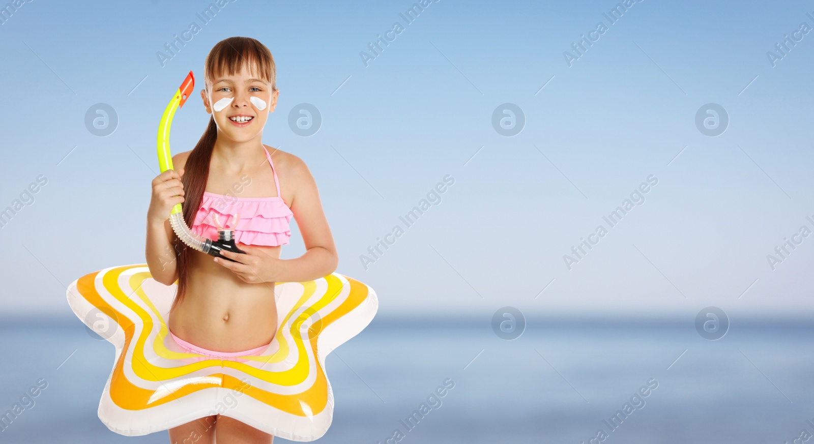 Image of Adorable little girl with sun protection cream on face and inflatable ring at beach, space for text. Banner design