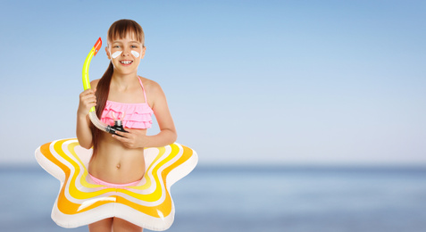 Image of Adorable little girl with sun protection cream on face and inflatable ring at beach, space for text. Banner design