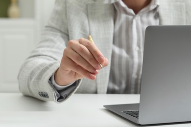 Photo of Man with pen and laptop at white table, closeup