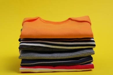 Stack of clean baby clothes on yellow background