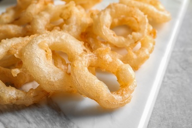 Photo of Closeup view of delicious golden breaded and deep fried crispy onion rings on marble board