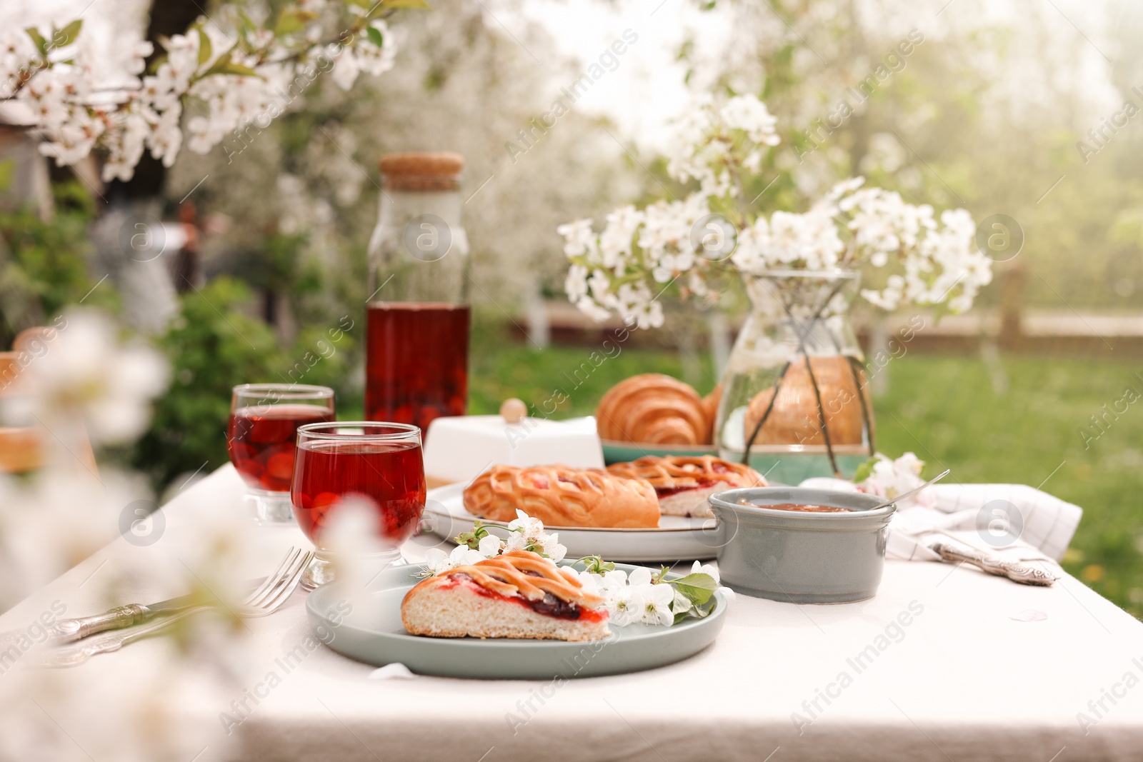 Photo of Stylish table setting with beautiful spring flowers, fruit drink and pie in garden