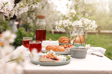 Stylish table setting with beautiful spring flowers, fruit drink and pie in garden