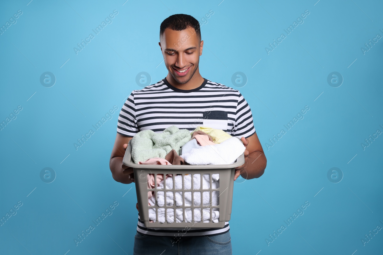 Photo of Happy man with basket full of laundry on light blue background