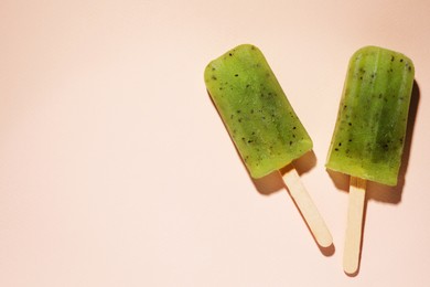Photo of Tasty kiwi ice pops and space for text on pale light pink background, top view. Fruit popsicle