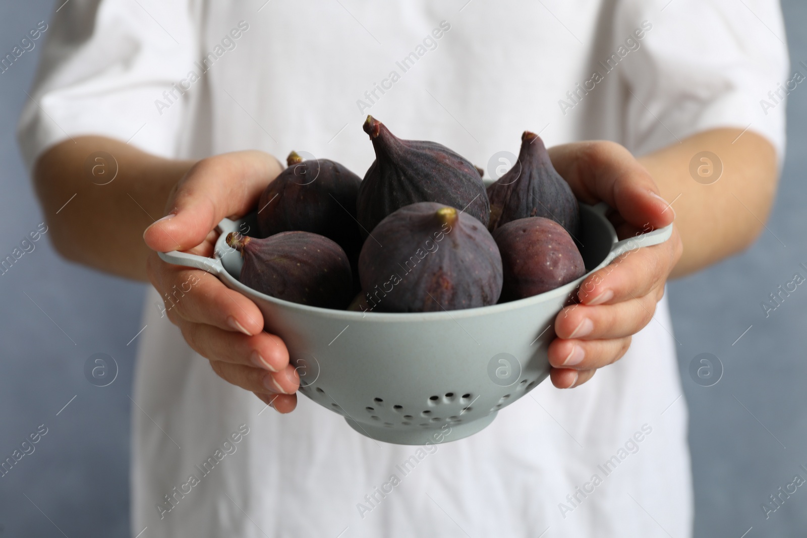 Photo of Woman holding colander with tasty raw figs on light blue background, closeup