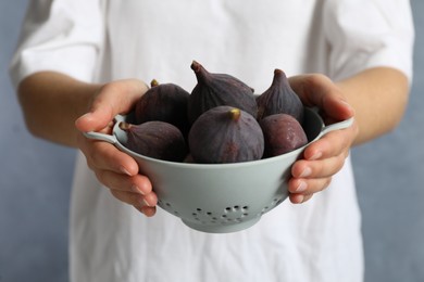 Woman holding colander with tasty raw figs on light blue background, closeup