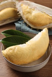Photo of Bowl with piece of fresh ripe durian and leaves on wooden table, closeup