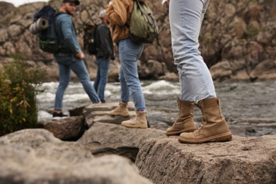 Photo of Group of friends with backpacks crossing mountain river, focus on hiking boots