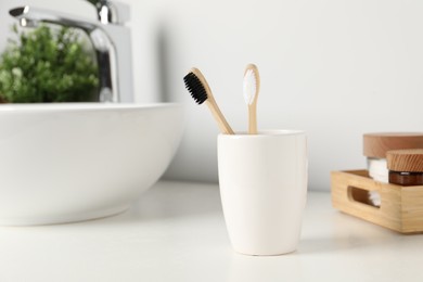 Photo of Bamboo toothbrushes on white countertop in bathroom