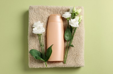 Soft folded towel with flowers and cosmetic product on green background, top view