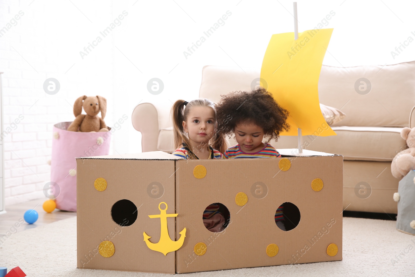 Photo of Cute little children playing with cardboard ship at home