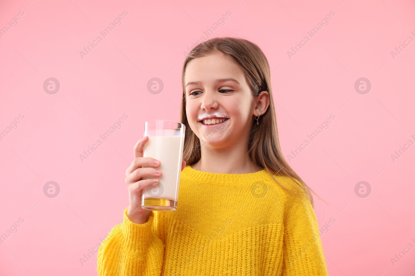 Photo of Happy little girl with milk mustache holding glass of tasty dairy drink on pink background