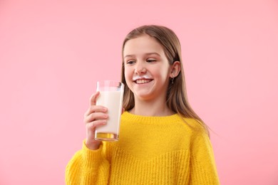 Happy little girl with milk mustache holding glass of tasty dairy drink on pink background