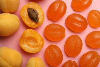 Delicious gummy apricot candies and fresh fruits on pink background, flat lay