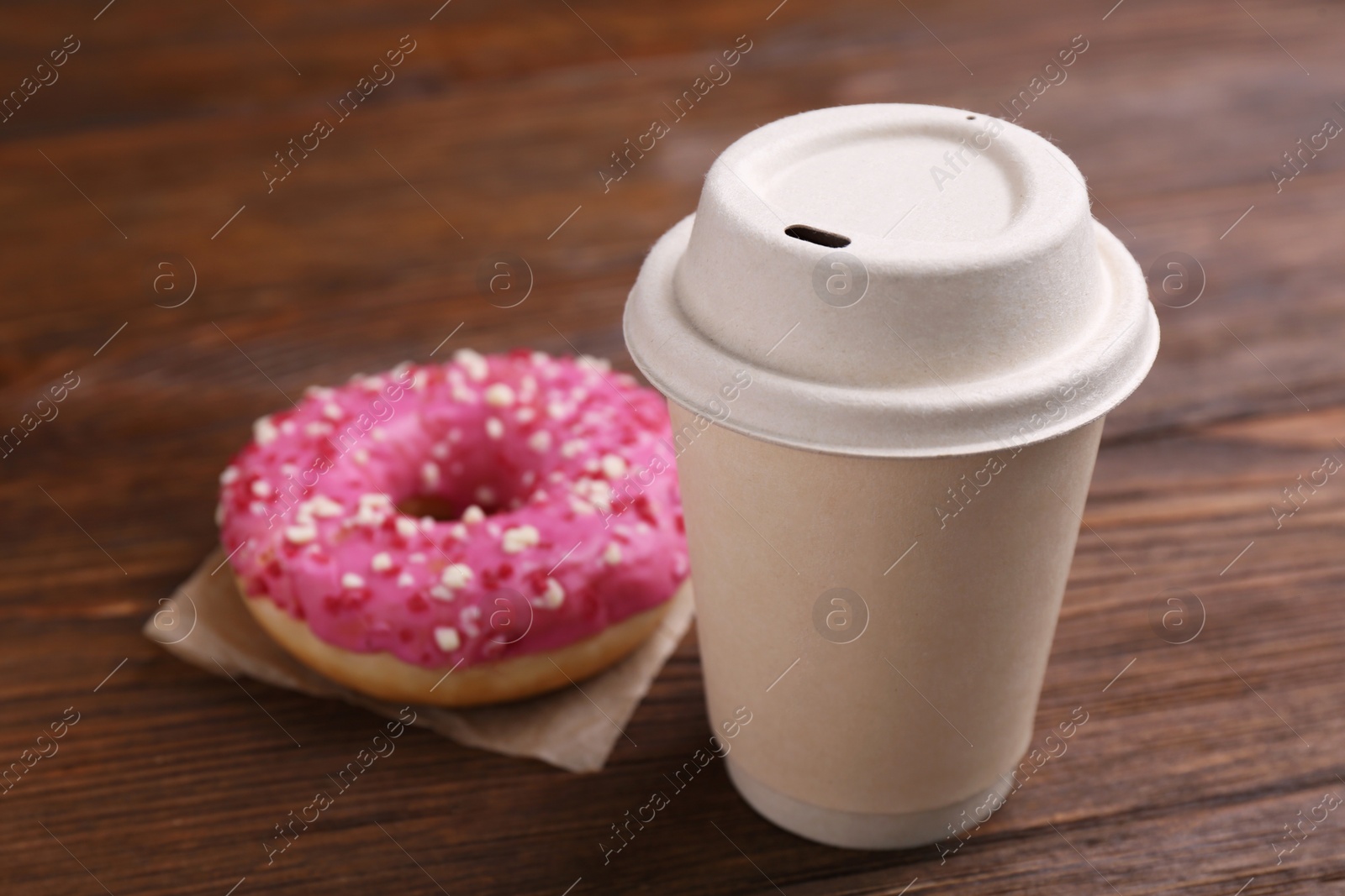 Photo of Tasty frosted donut with sprinkles and hot drink on wooden table