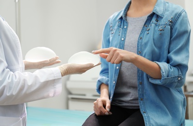 Doctor showing silicone implants for breast augmentation to patient in clinic, closeup. Cosmetic surgery